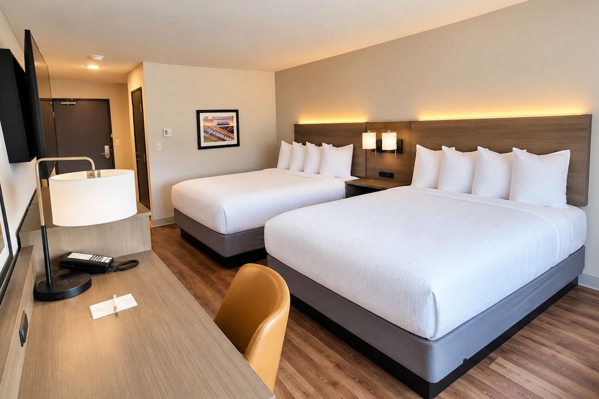 Une chambre d’hôtel avec deux lits, un bureau avec une lampe, une chaise et un téléviseur.