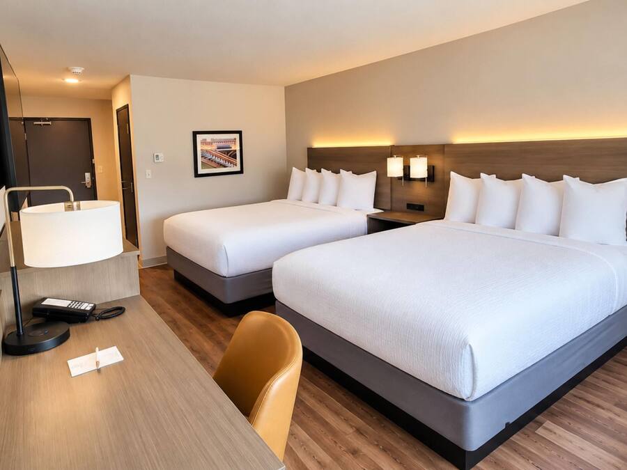 Habitación de hotel con dos camas, un escritorio con lámpara, una silla y un televisor.