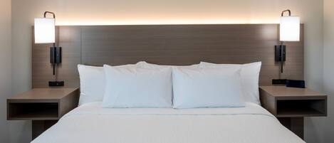 Quarto de hotel com uma cama grande, duas mesinhas de cabeceira e luminárias fixadas na parede.