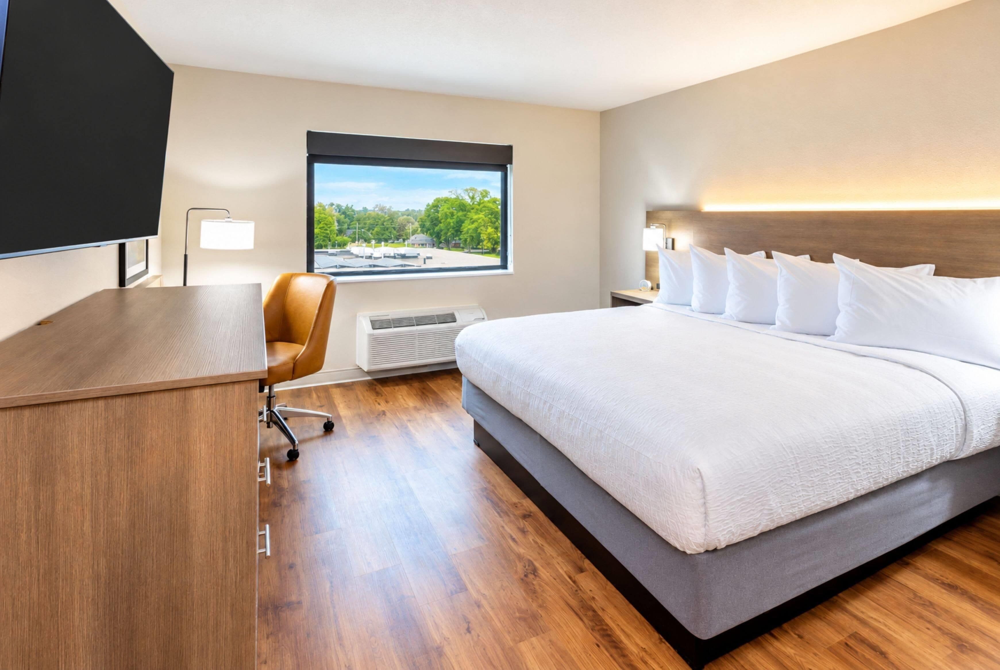Habitación de hotel con cama, escritorio, silla y ventana con vistas a la vegetación.