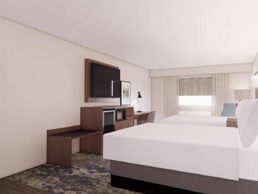 A hotel room with a large bed, a desk, a TV, and a mirror.