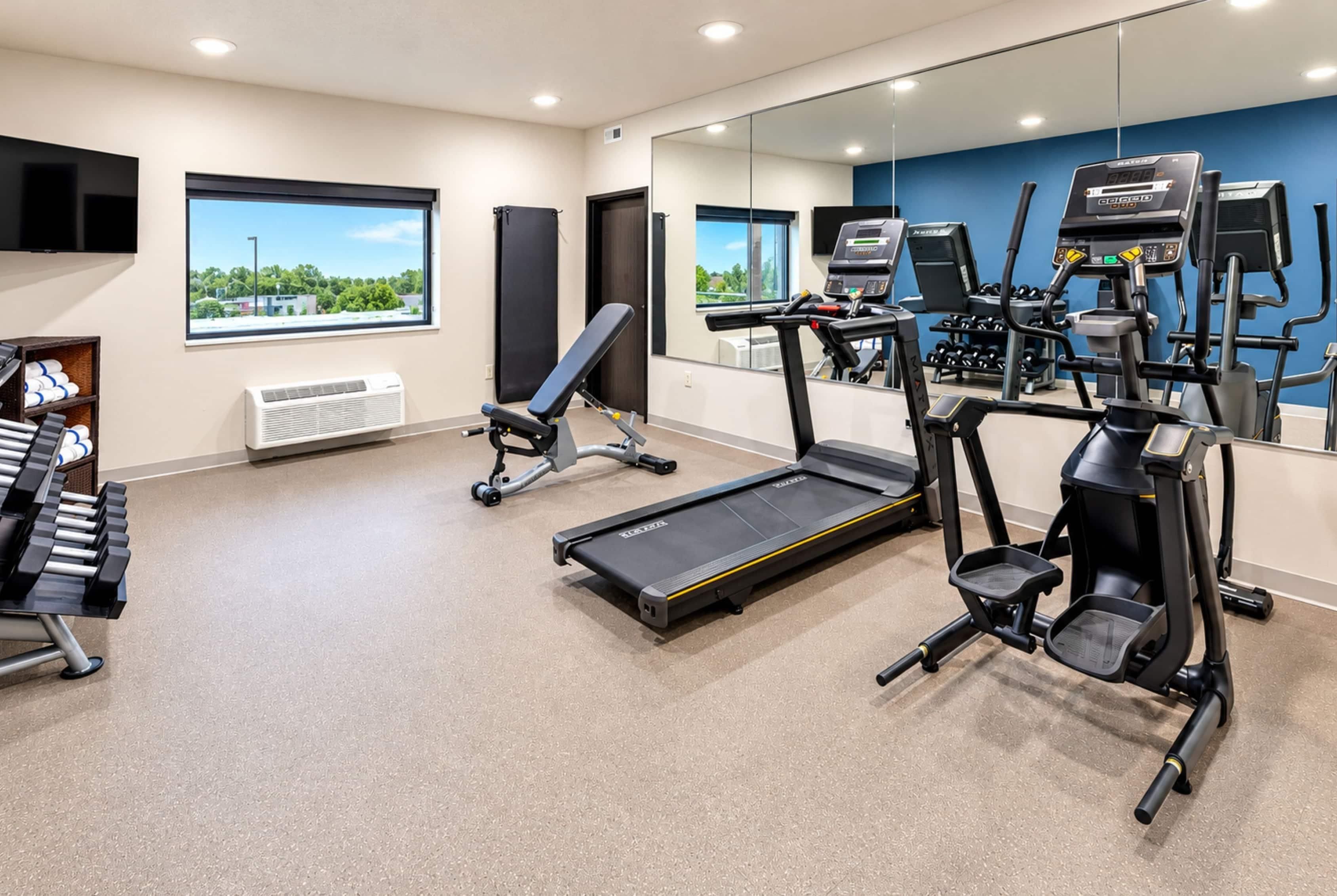 Une salle de sport équipée de tapis de course, d’un banc de musculation et d’un téléviseur fixé au mur.