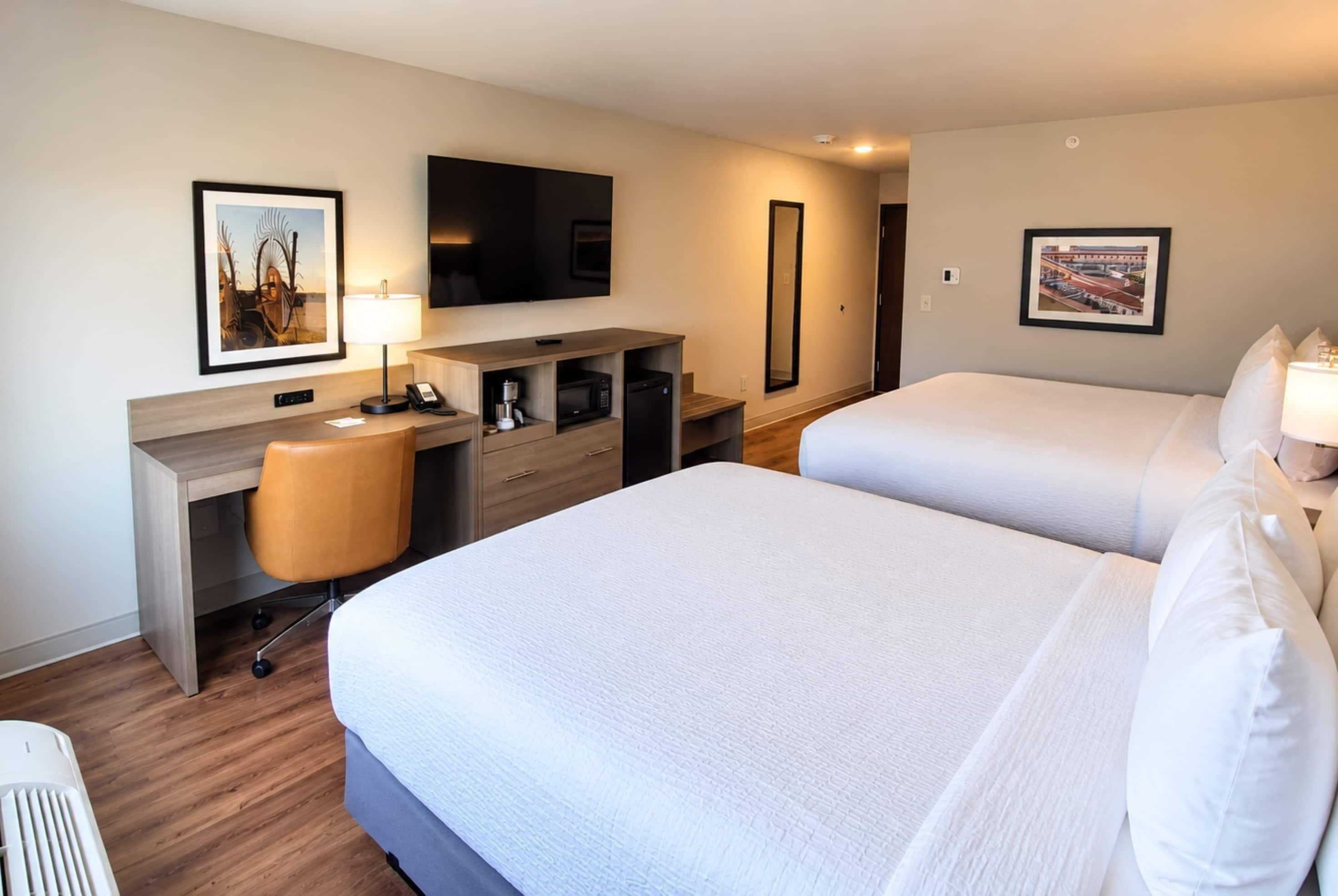 A hotel room with two beds, a desk with a chair, a television, a coffee machine, and artwork on the walls.