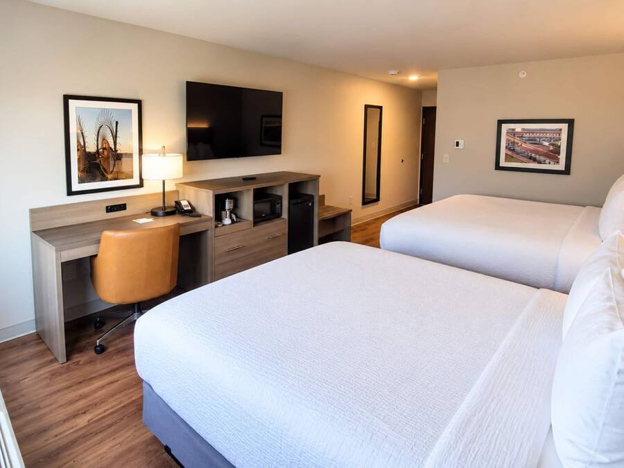 A hotel room with two beds, a desk with a chair, a television, a coffee machine, and artwork on the walls.
