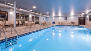 Una piscina interna con acqua cristallina, circondata da sdraio e tavolini.