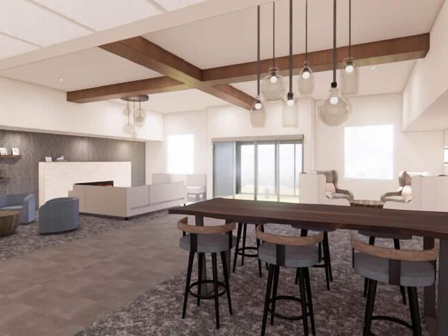 A spacious, modern interior with a long wooden table and bar stools, a seating area with sofas, and a kitchen area with a countertop and shelving.
