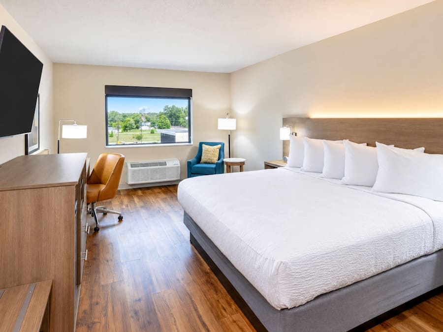 A hotel room with a large bed, a desk, a chair, a TV, and a window with a view.