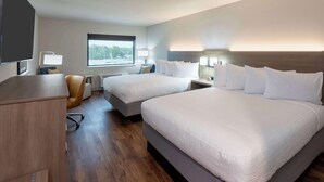 Camera d'albergo con due letti, una scrivania, una sedia e un'ampia finestra.
