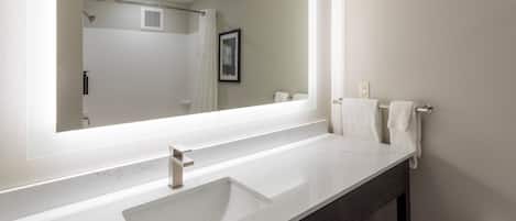 A modern bathroom with a large mirror, white sink, and dark wooden vanity.