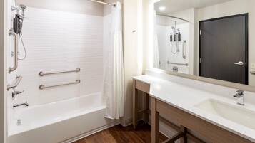 Un baño moderno con cabina de ducha, barras de apoyo, tocador con espejo y suelo de madera.