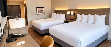 A hotel room with two beds, a desk with a lamp, a TV, and a picture on the wall.
