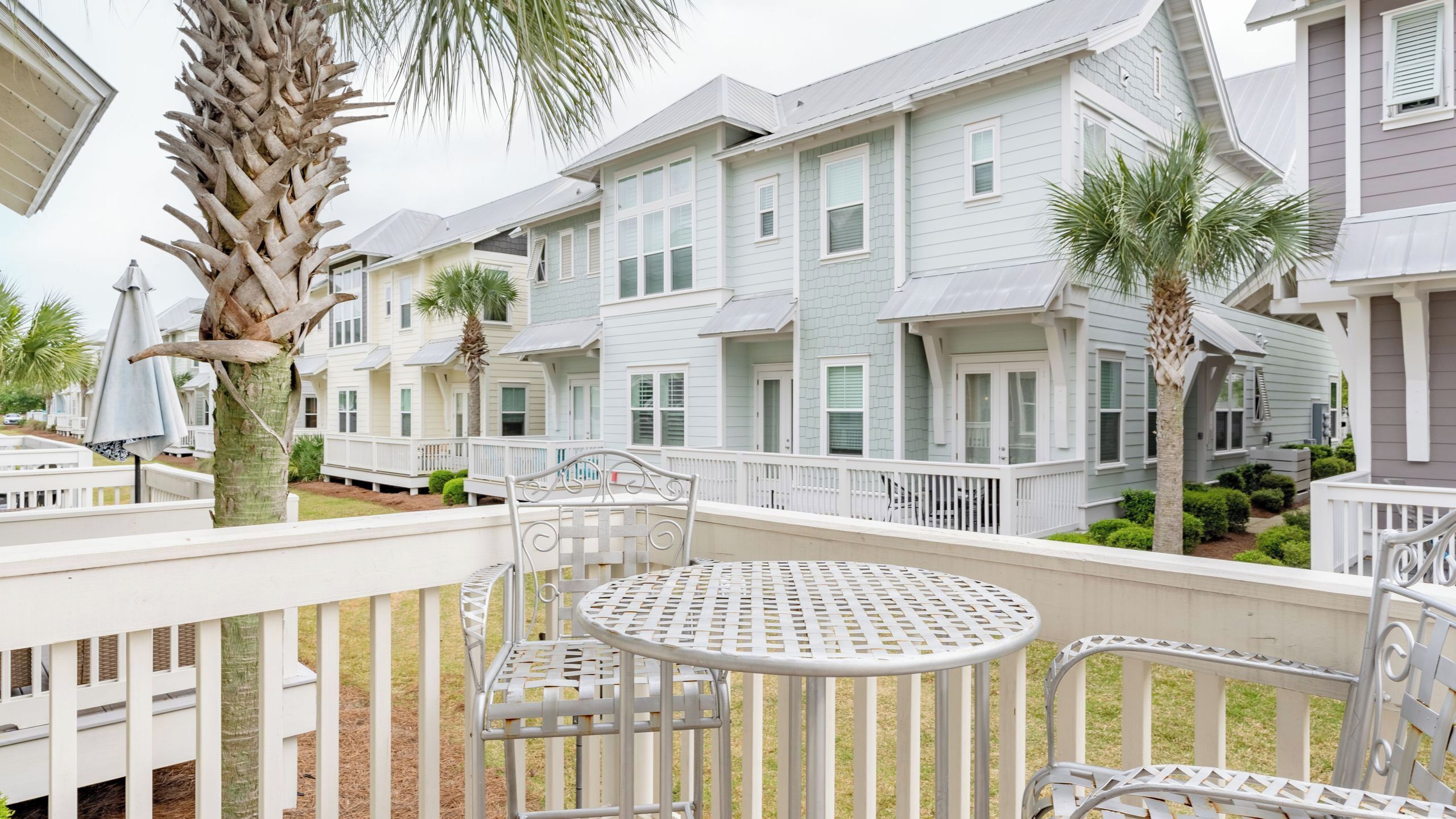 A residential area with multiple-story houses, a fenced deck with metal chairs, and a palm tree.