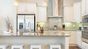 A modern kitchen with white cabinets, granite countertops, stainless steel appliances, and bar stools. - Emerald Gem by Avantstay Pool Access, 3mins to Beach! (Santa Rosa Beach)