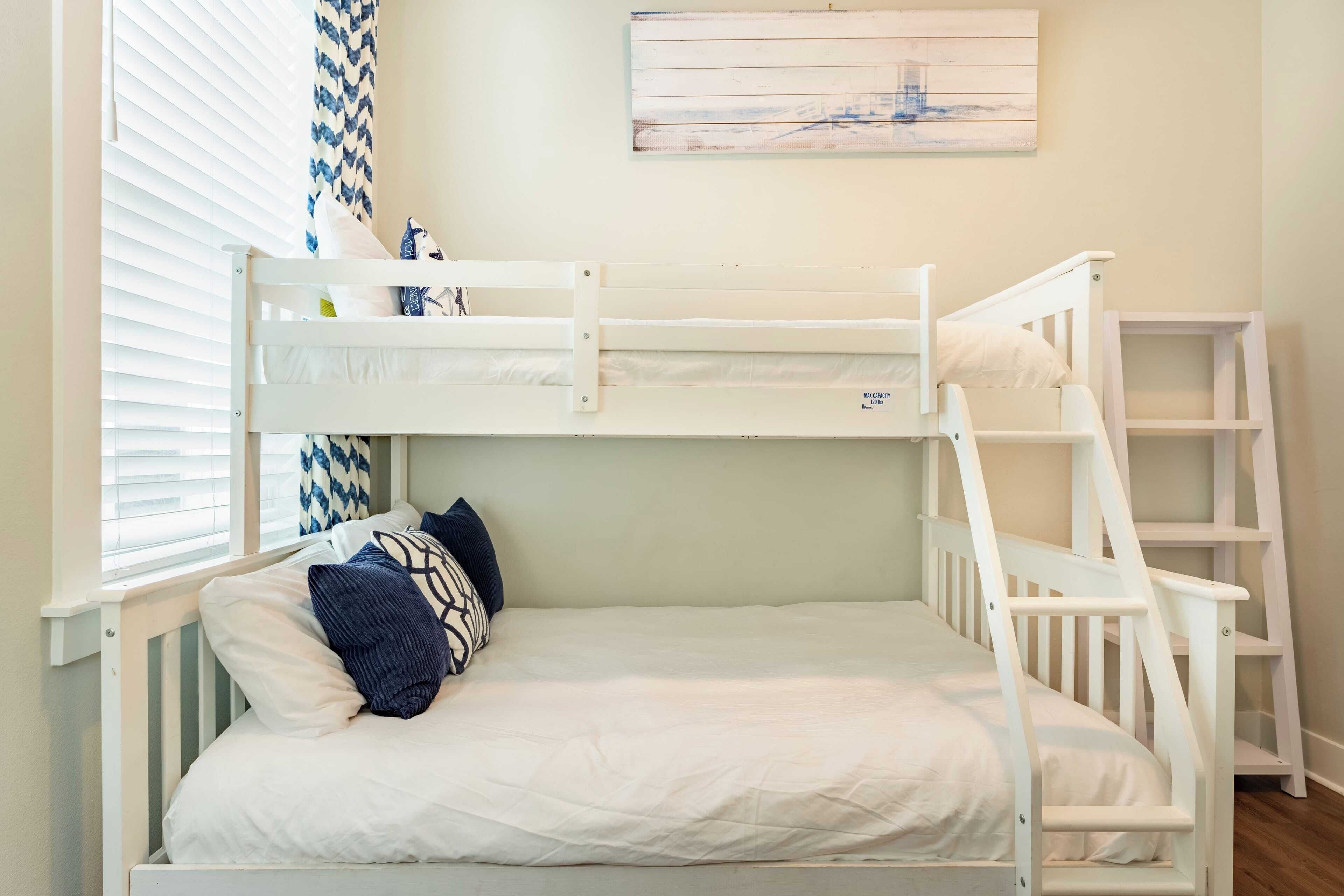 Una cama litera con estructura blanca, una cama inferior con colchón blanco y almohada azul, y una escalera en el lado derecho.