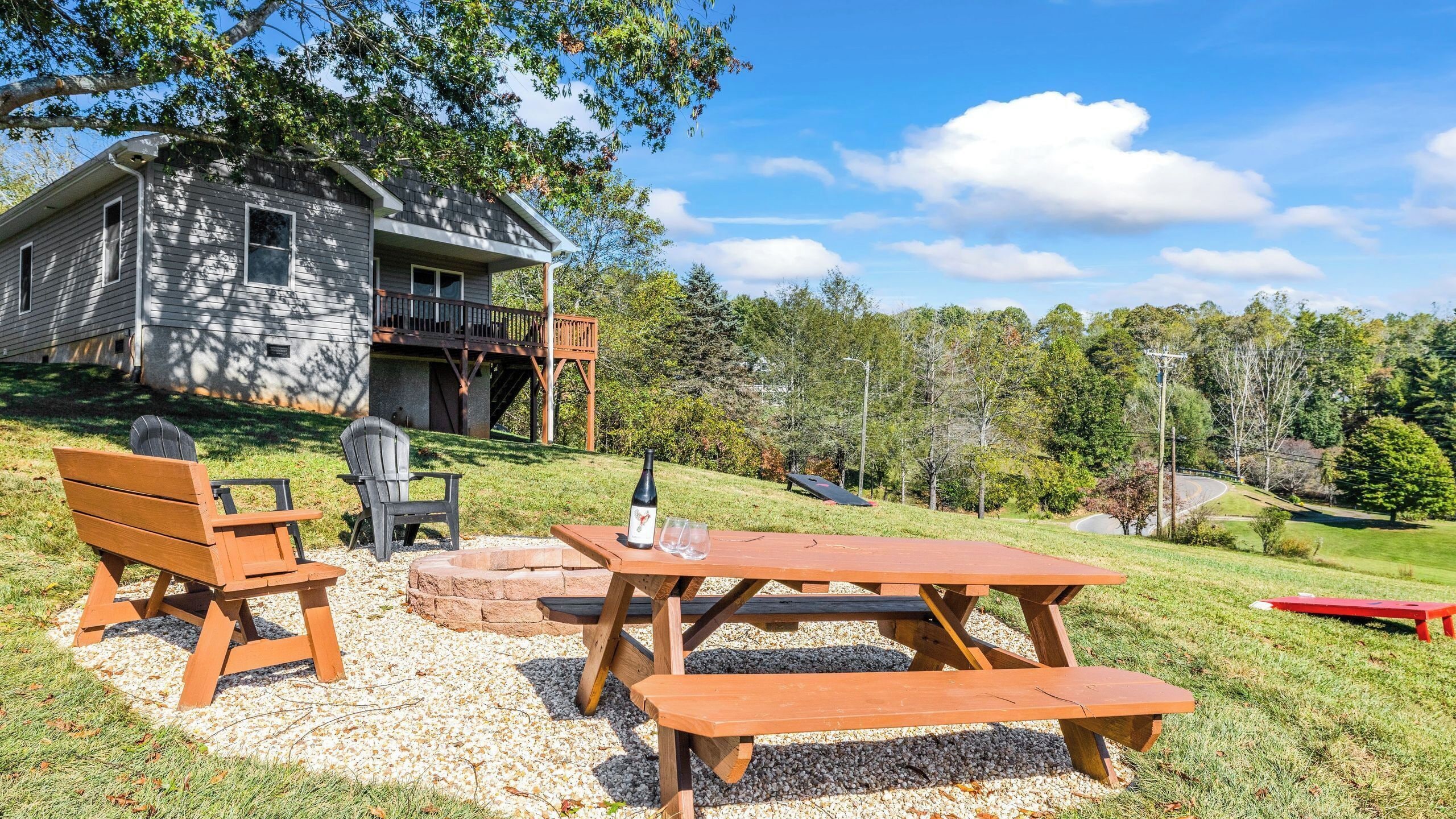 A house with a deck, a picnic table, and two Adirondack chairs.