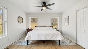 A bedroom with a bed, a ceiling fan, two windows, a door, and a patterned rug.