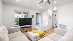Ein modernes Wohnzimmer mit Flachbildfernseher, weißen Sofas, einer Holz-Unterhaltungseinheit und einem Deckenventilator.