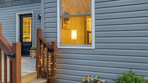 Ein Haus mit einer hölzernen Veranda, einer schwarzen Tür und einem Fenster mit gelbem Innenlicht.