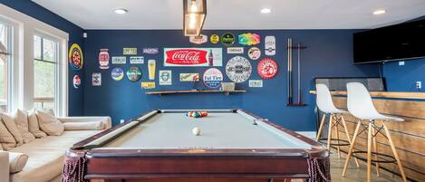 Ein Billardtisch in einem Raum mit blauer Wand, einer Couch und einer Bar.