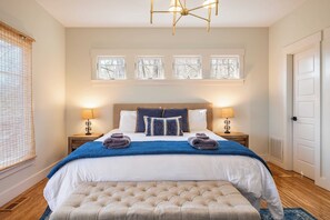 Une chambre à coucher bien rangée, avec un grand lit, deux tables de chevet avec des lampes, une fenêtre avec des stores et une porte.