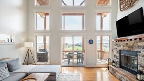 Een ruime woonkamer met een grote televisie, een open haard en een balkon met zitplaatsen.