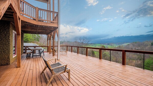 A wooden deck with a table and chairs, a covered area with a railing, and a scenic view of a valley.