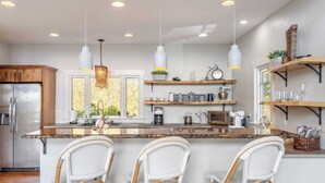 A modern kitchen with a central island, bar stools, hanging pendant lights, and built-in shelves with kitchenware. - Private Retreat w/ Hot Tub, Amazing Views, Game Room Silver Spoon by Avantstay (Leicester)