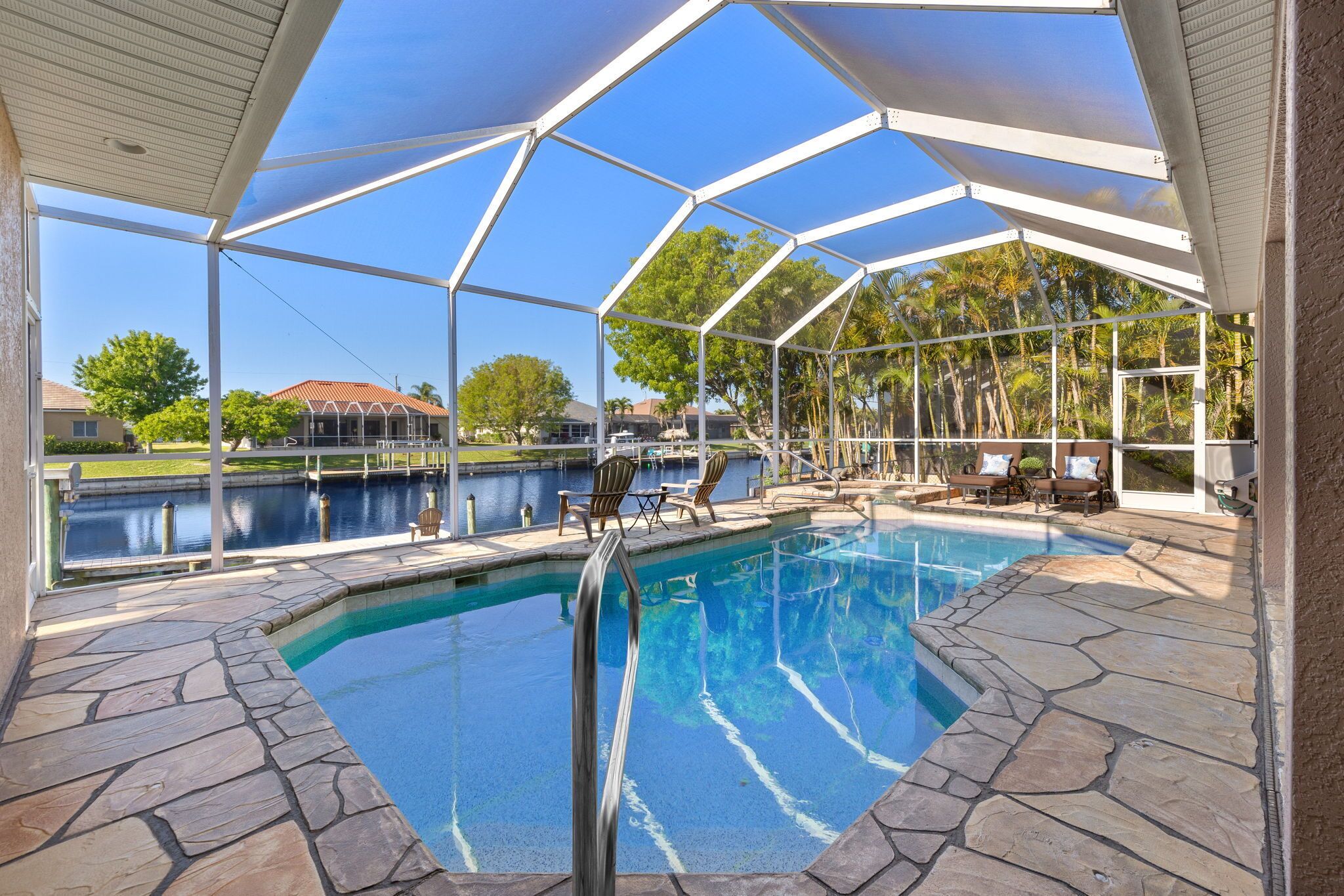 A covered swimming pool with stone flooring, lounge chairs, and a view of a lake and buildings.