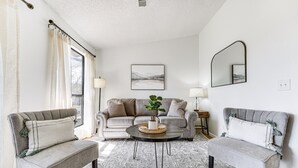 A living room with a sofa, two armchairs, a coffee table with a plant, and a large window with curtains. - 5 Mi to Strip! Pointe Royale Condo w/ Indoor Pool (Branson)