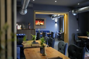 Un restaurant moderne doté d’une cheminée centrale, de sièges rembourrés en tissu bleu et d’une table à manger en bois.