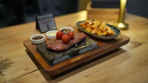 Een steak met kersentomaten en friet op een houten plank, vergezeld van kleine schaaltjes met sauzen.