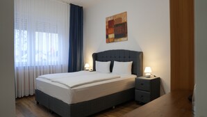 Een net opgemaakt bed met witte lakens, een donker hoofdbord en twee bedlampjes.