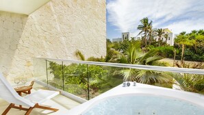 Un balcón con bañera de hidromasaje, pared de piedra y vista a palmeras y edificios.