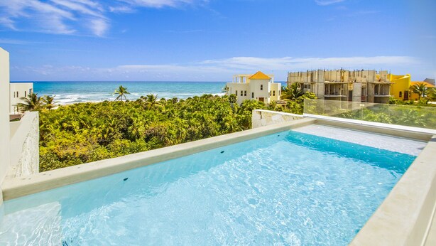Una piscina infinita en la azotea con vistas al océano y vegetación tropical.
