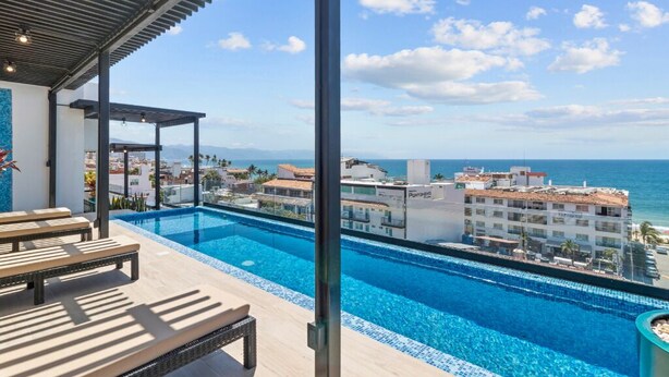 A rooftop infinity pool with a clear view of the ocean and surrounding buildings.