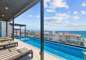 A rooftop infinity pool with a clear view of the ocean and surrounding buildings.