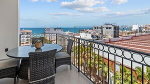 A balcony with a round table and chairs, overlooking a coastal cityscape with buildings and the sea.