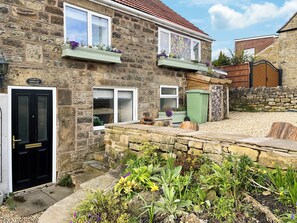 A stone cottage with a black door, windows, and a small garden with various plants.