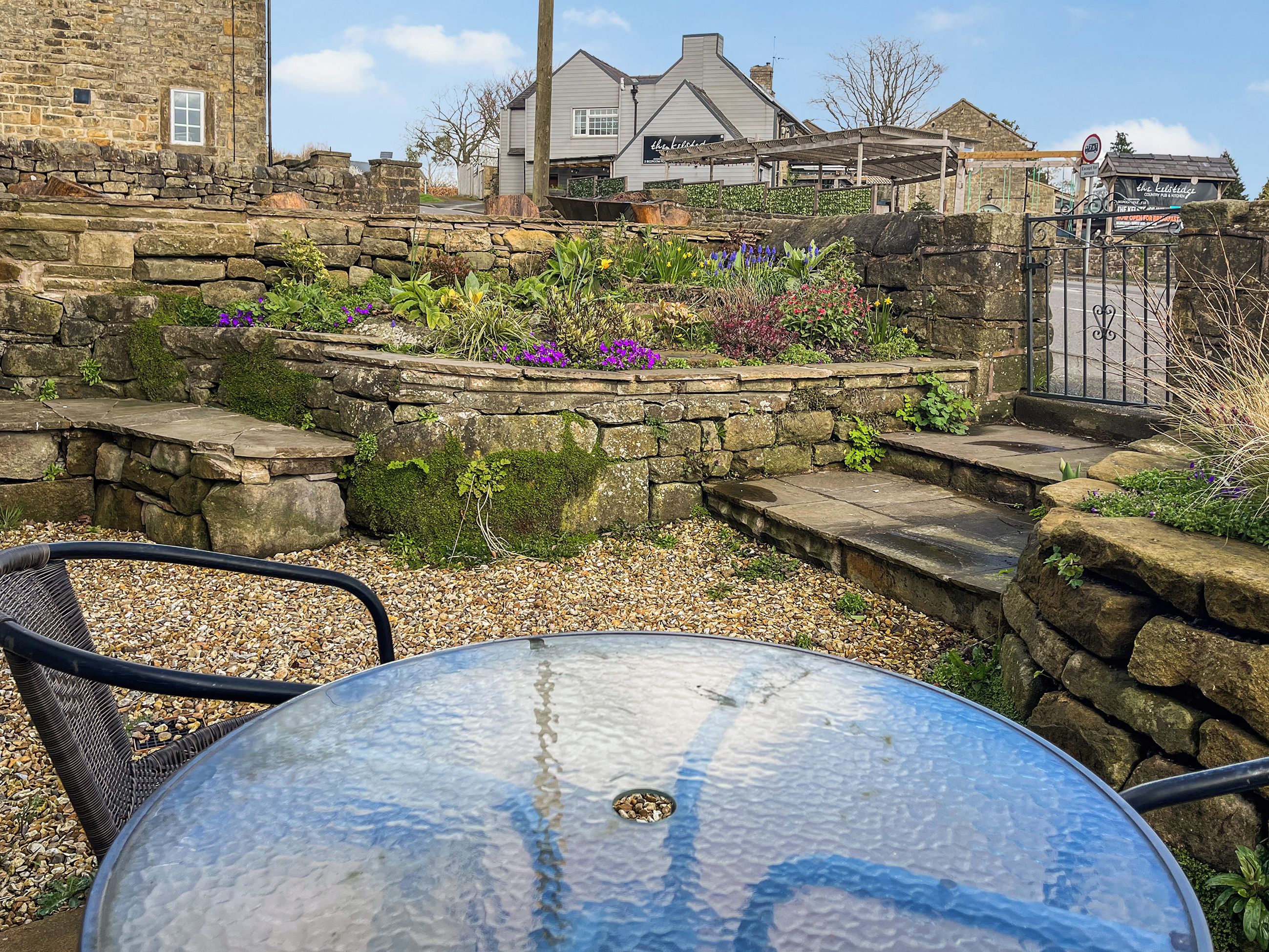 A stone wall with a garden in front of a building with a sign that reads "the kitchen."