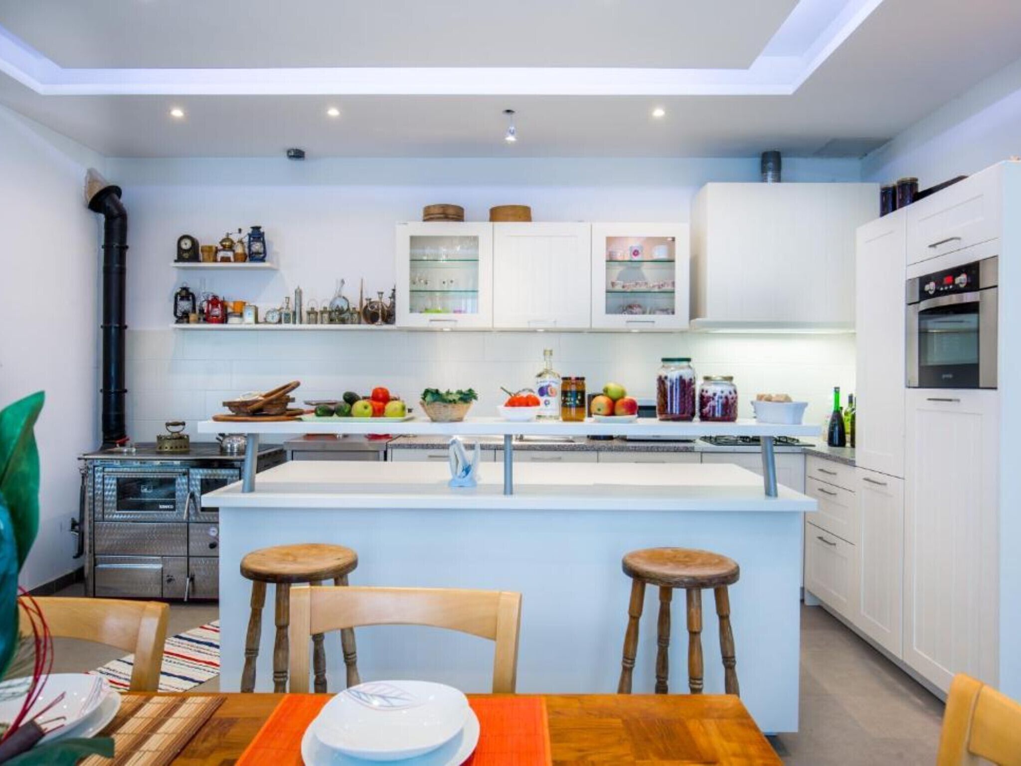 A modern kitchen with white cabinets, a central island with stools, and a dining area with a table and chairs.