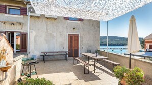 Une terrasse extérieure avec une table et des chaises, un barbecue et des plantes en pot.