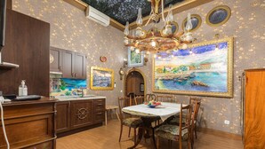 A dining area with a wooden table and chairs, a chandelier, and a large framed painting of a coastal scene.