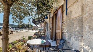 An outdoor seating area with a table and chairs, surrounded by potted plants and a tree.