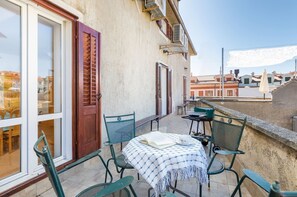 Un balcón al aire libre con mesa y sillas, una puerta y vistas a la ciudad.