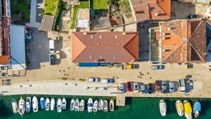 An aerial view of a coastal area with a marina, boats, and buildings with red-tiled roofs.