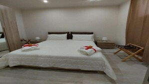 A neatly made bed with white linens and two towels, a wooden nightstand with a lamp, and a folding chair. - The Two Pine Cones Palermo (Palermo)