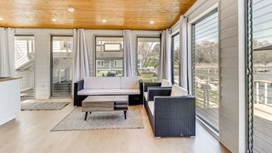 Een moderne woonkamer met een houten plafond, grote ramen, een bank en een eettafel.