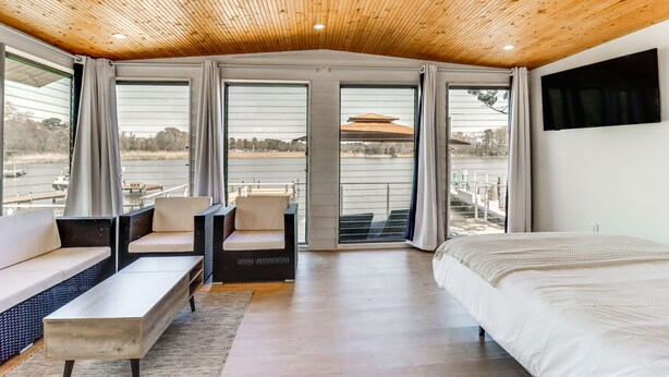 Een slaapkamer met een groot bed, een bank en een stoel, met uitzicht op een waterpartij en een gebouw op de achtergrond.