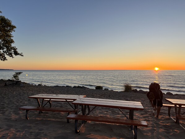 A beach with picnic tables and a sunset over the water. - Home in Downtown Empire! Walk to the beach! (Empire)