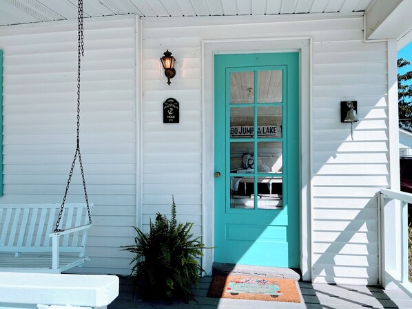 A white house with a turquoise door, a porch swing, and a small potted plant.